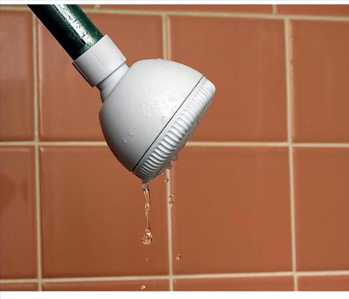 a white plastic shower head attached to a rusty metal pipe is leaking, bathroom wall tiles are in the background